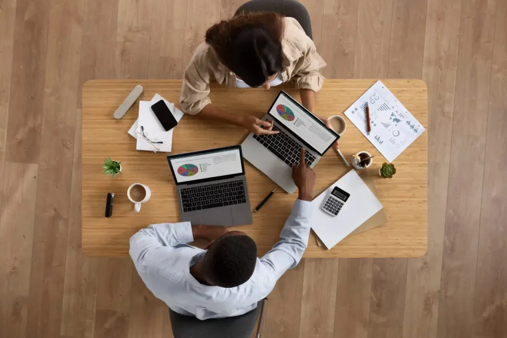 Une jeune fille et un jeune homme autour d'un bureau, avec des ordinateurs et des paperasses