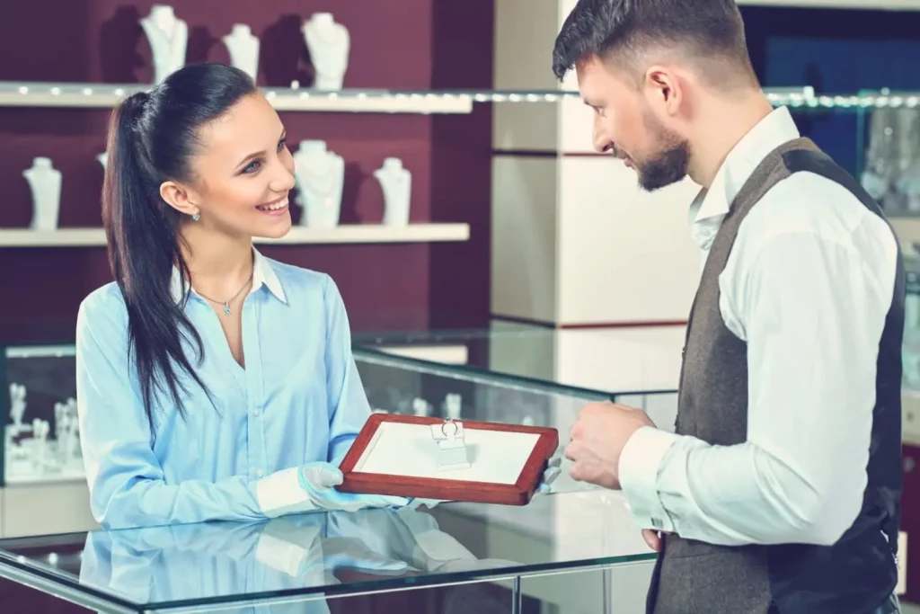 Une jeune femme qui reçoit un client en bijouterie avec un sourire et un air professionnel.