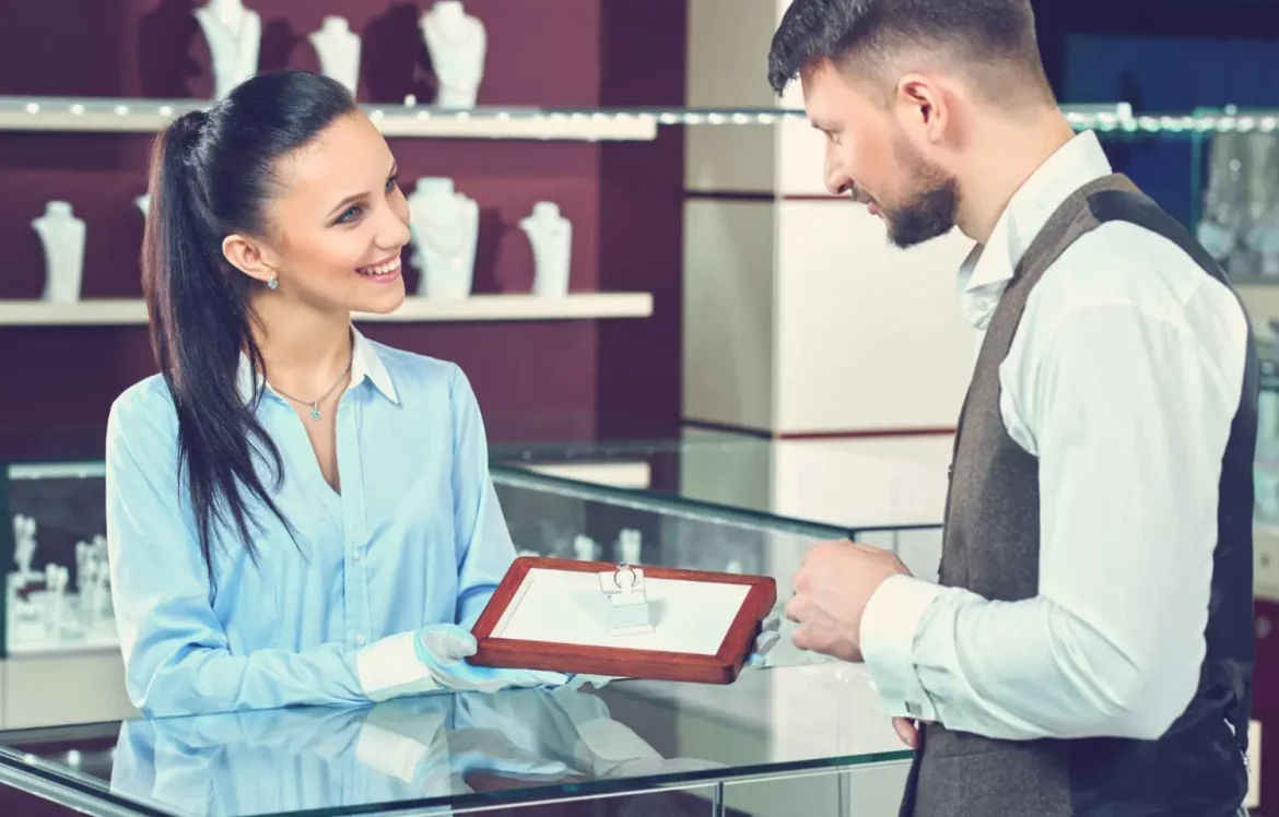 Une jeune femme qui reçoit un client en bijouterie avec un sourire et un air professionnel.