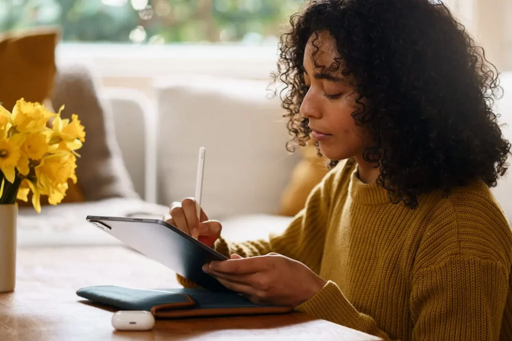 Une jeune fille aux cheveux bouclés qui travaille sur sa tablette avec un stylet.