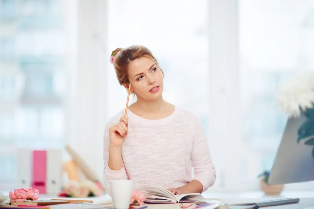 Une jeune fille qui travaille sur son bureau, tient un crayon entre les mains et est pensive