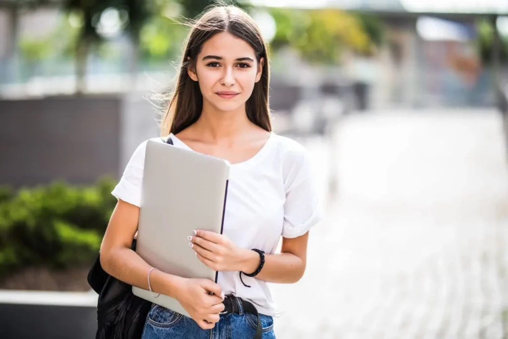 Une étudiante qui tient son ordinateur portable à l'extérieur de l'université