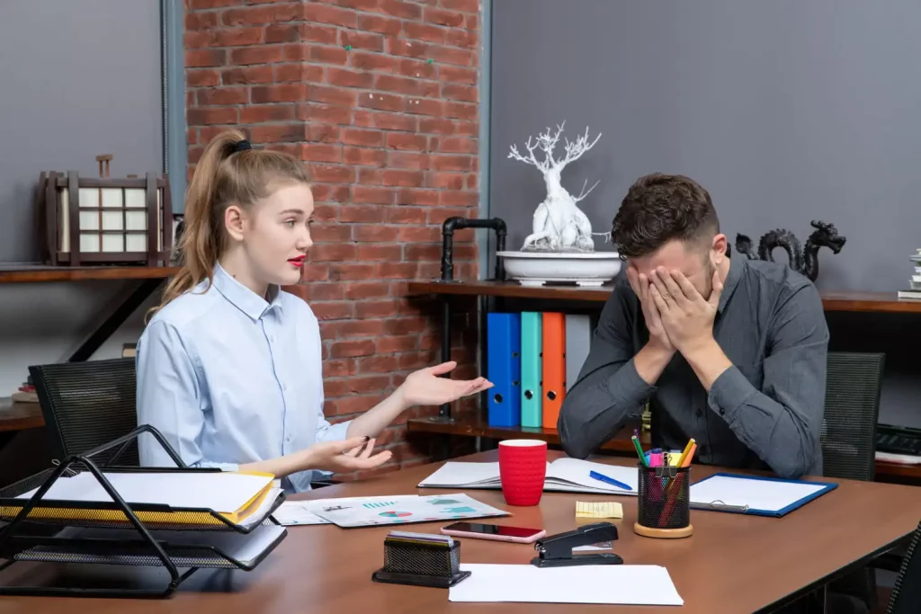 Un homme et une femme discutent au bureau, l'un se plaint et l'autre se cache le visage