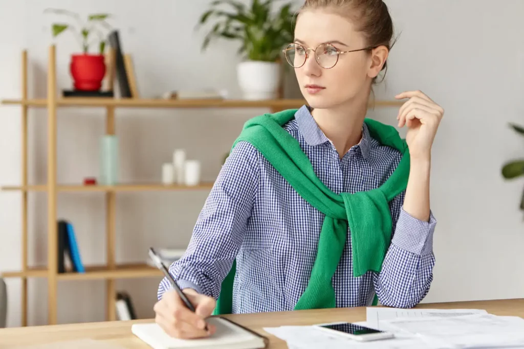 Une femme pensive tenant un stylo et travaillant sur son bureau