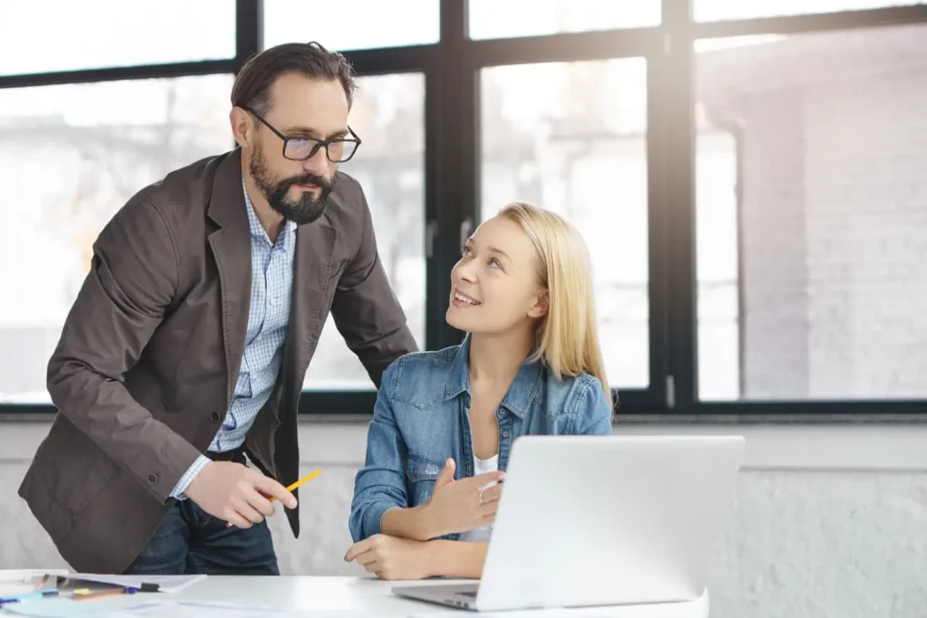 Un tuteur explique ses tâches à une nouvelle apprenti de l'entreprise, devant l'ordinateur