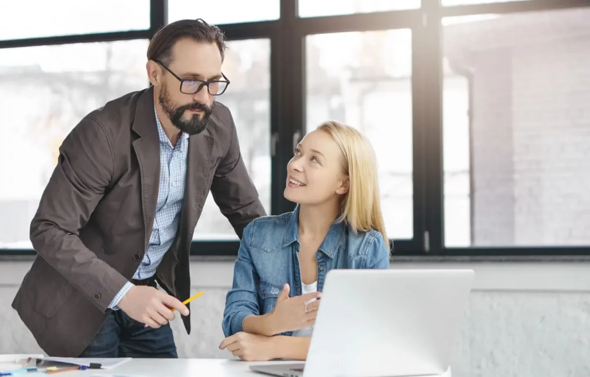 Un tuteur explique ses tâches à une nouvelle apprenti de l'entreprise, devant l'ordinateur